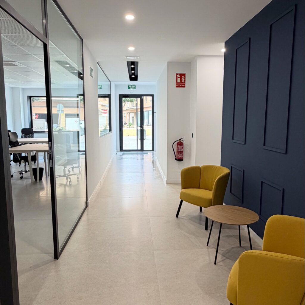 Zona de espera en la entrada de Lola Coworking Calle Lima, con sillas y logotipo en la pared